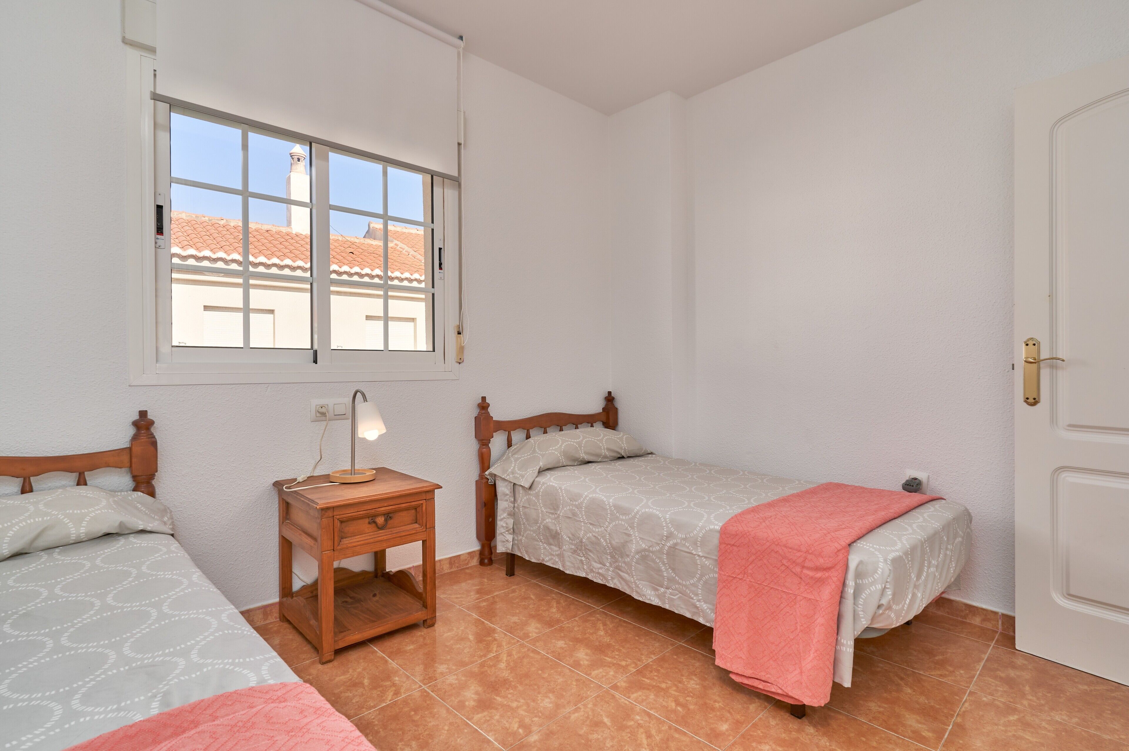 A bedroom with two beds, a nightstand, a window, and a door.