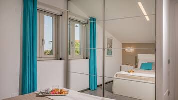 A bedroom with a bed, a bedside table with a tray of food, a window with curtains, and a mirror reflecting the room.