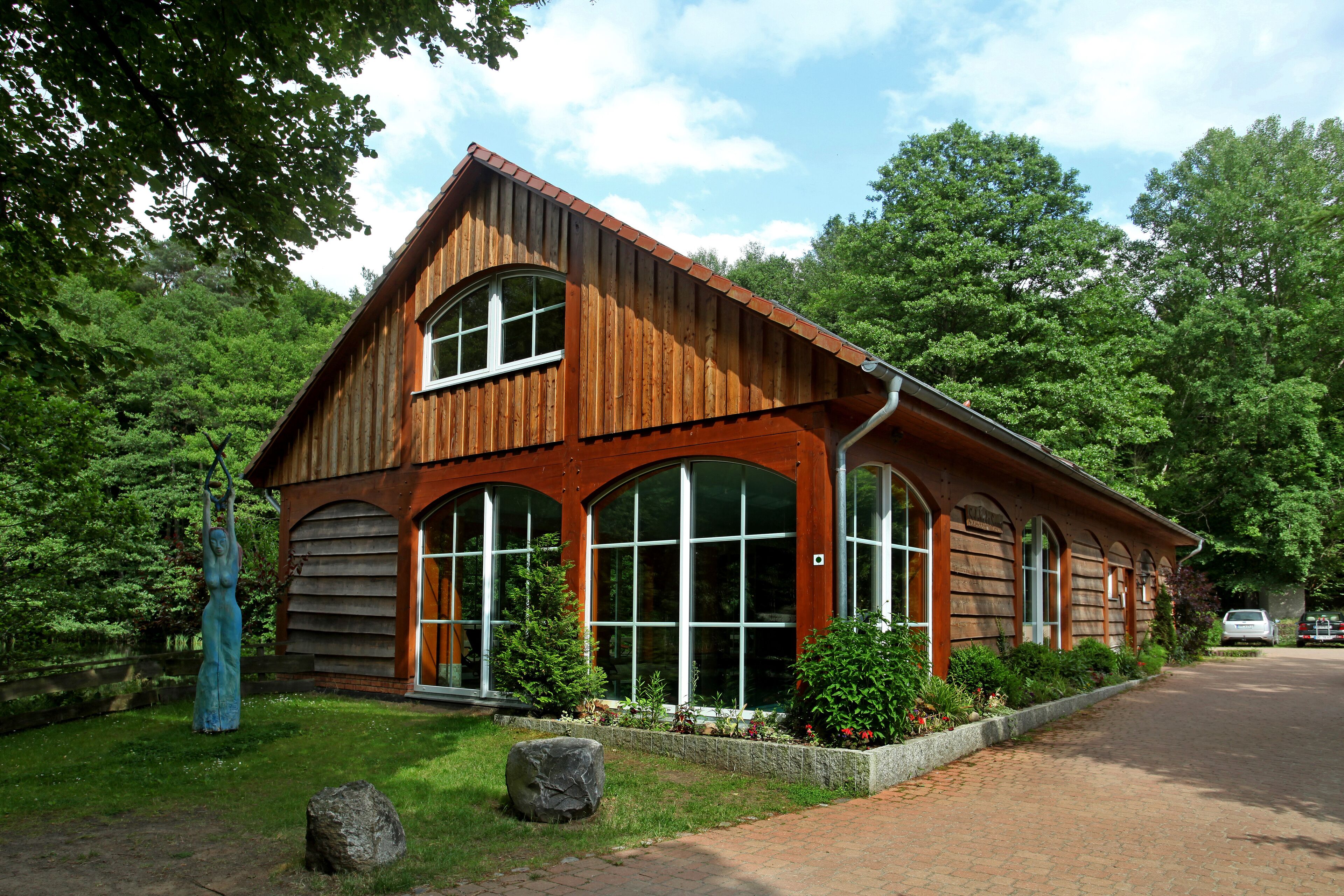 A wooden cabin with large arched windows and a sloped roof, surrounded by lush greenery.