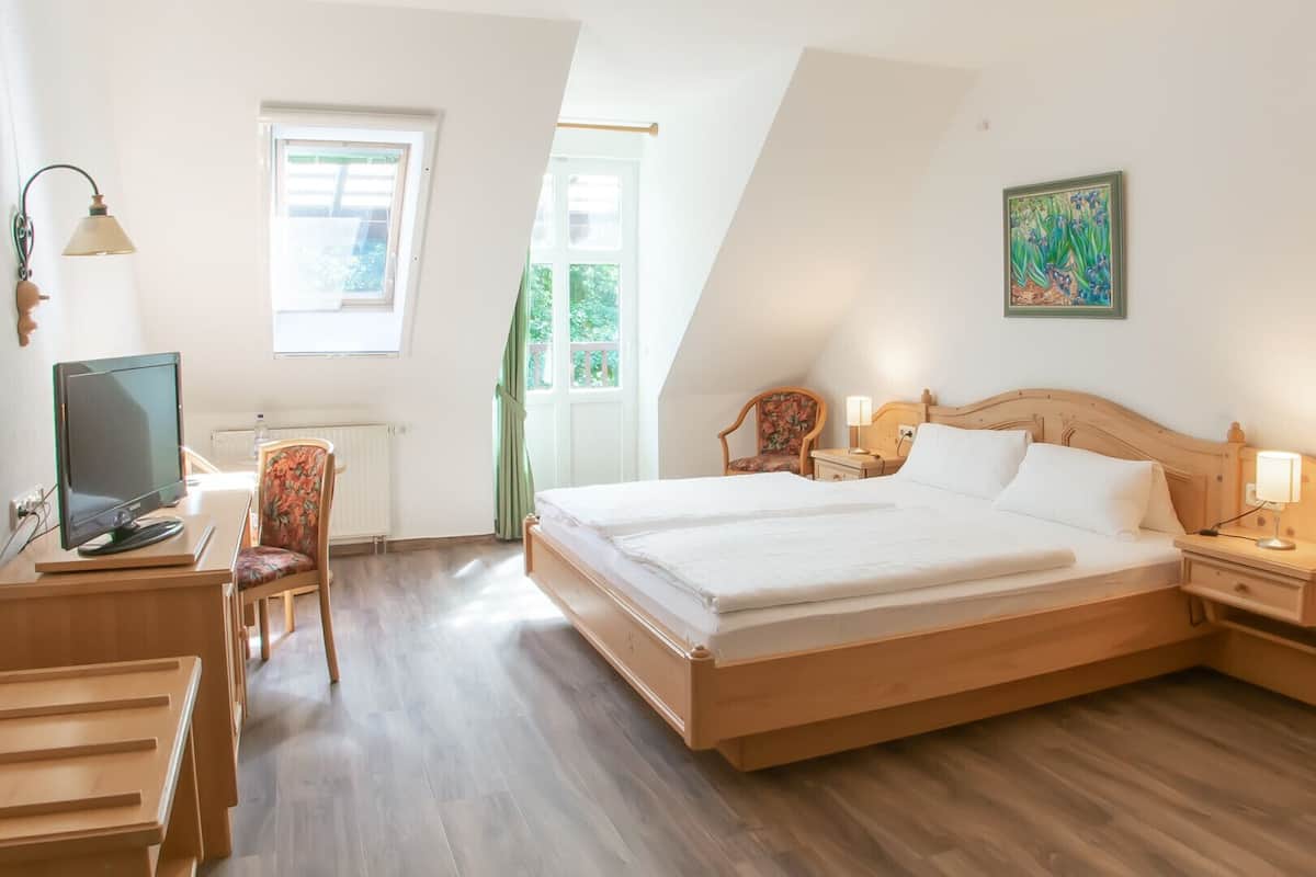 Een slaapkamer met een bed, nachtkastjes, een bureau met stoel, een televisie en een raam.