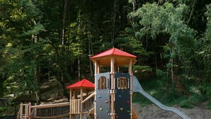Une aire de jeux avec des structures d’escalade, des toboggans et une cabane en bois.