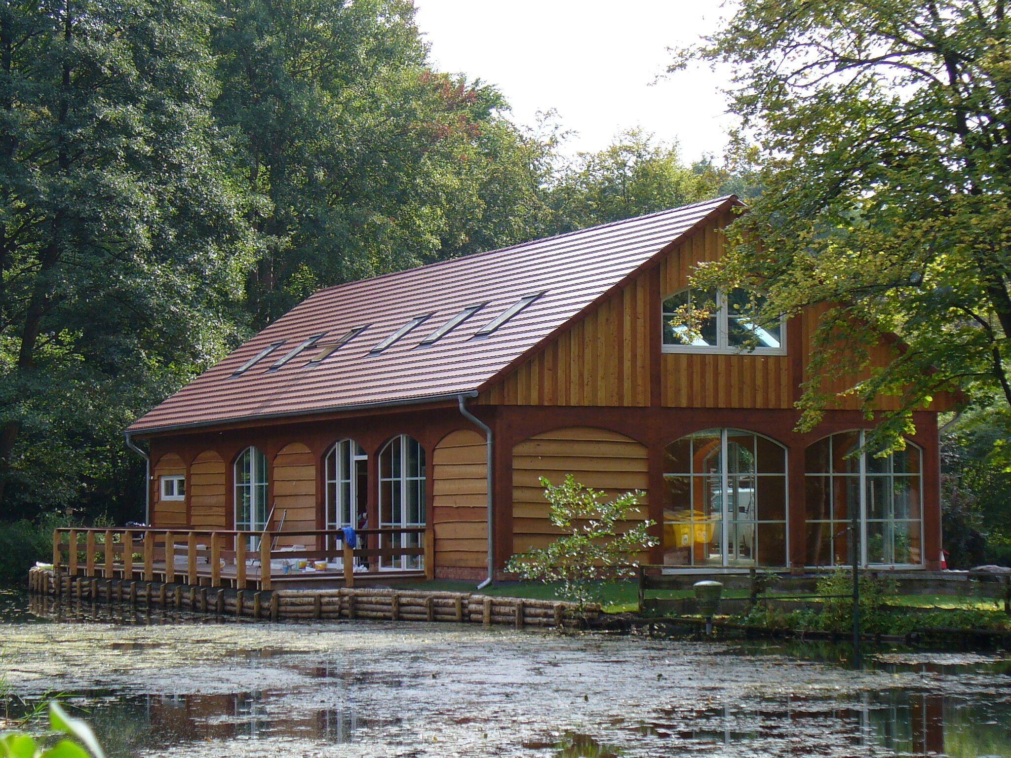 A wooden building with a sloped roof and large windows, situated by a body of water.