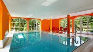 Une piscine intérieure aux murs orange, offrant une vue dégagée sur la verdure environnante.