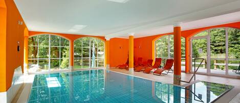 An indoor swimming pool with orange walls and a clear view of greenery outside.