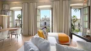 Une chambre d’hôtel avec un balcon, un coin repas et une vue sur un immeuble orné d’une statue.