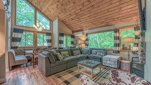 A cozy living room with a large sectional sofa, a patterned rug, and a wooden ceiling.