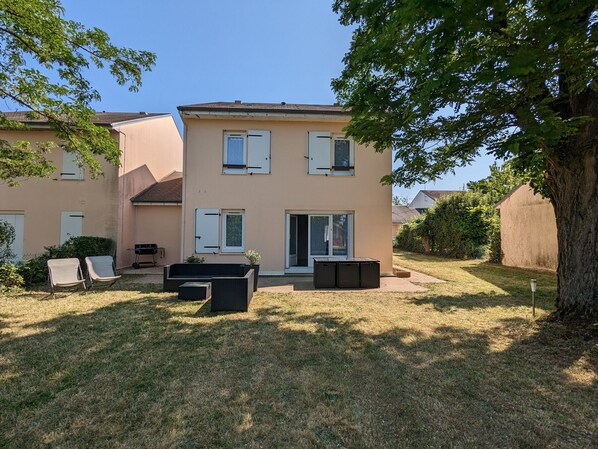 Un bâtiment à deux étages doté d’un toit plat, d’une porte-fenêtre coulissante et d’un petit espace patio aménagé avec du mobilier d’extérieur.