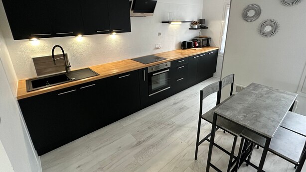 Une cuisine moderne avec des meubles de couleur noire, un plan de travail en bois et un four encastré.