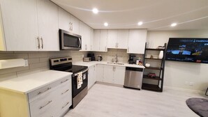 Una cocina moderna con armarios blancos, electrodomésticos de acero inoxidable y un televisor de pantalla plana mostrando un evento deportivo.