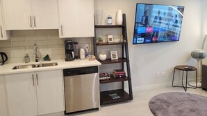 Una cocina moderna con lavavajillas, cafetera y televisor montado en la pared mostrando la pantalla de inicio.