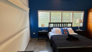 A bedroom with a bed, a nightstand, a window with blinds, and an air conditioner.