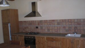 Una cocina con gabinetes de madera, estufa a gas, horno, lavamanos y salpicadero de azulejos.
