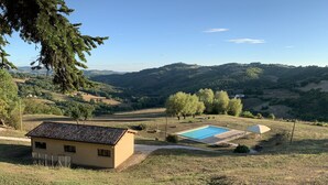 Paisaje rural con una casa pequeña, una piscina y una tienda de campaña.