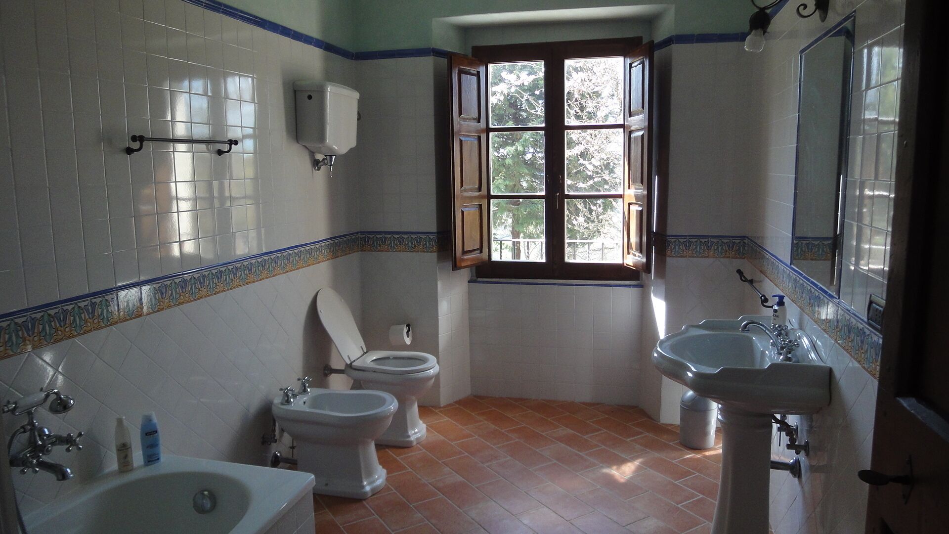 Une salle de bain avec deux toilettes, un bidet, un lavabo et une fenêtre donnant sur les arbres.