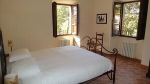 Un dormitorio con cama, dos ventanas, un radiador y una silla.