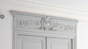 Une porte à deux battants, de couleur blanche, ornée de sculptures complexes et dotée de poignées en laiton.