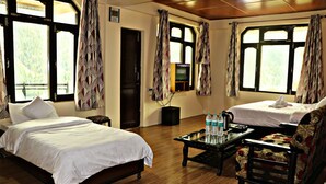 A hotel room with two beds, a coffee table with water bottles, a TV, and a view of a mountainous landscape. - Hotel Prakash Regency Sangla (Sangla)