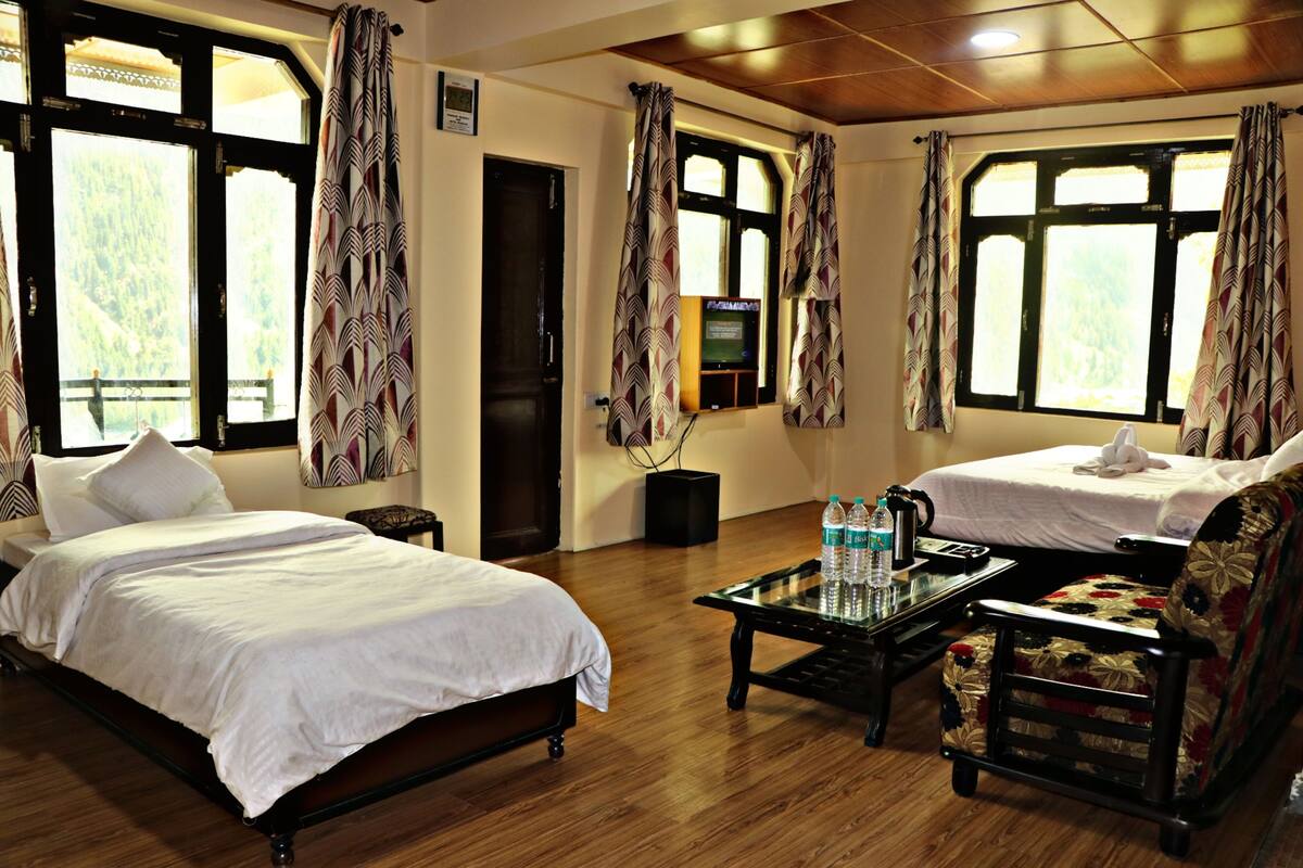 A hotel room with two beds, a coffee table with water bottles, a TV, and a view of a mountainous landscape.
