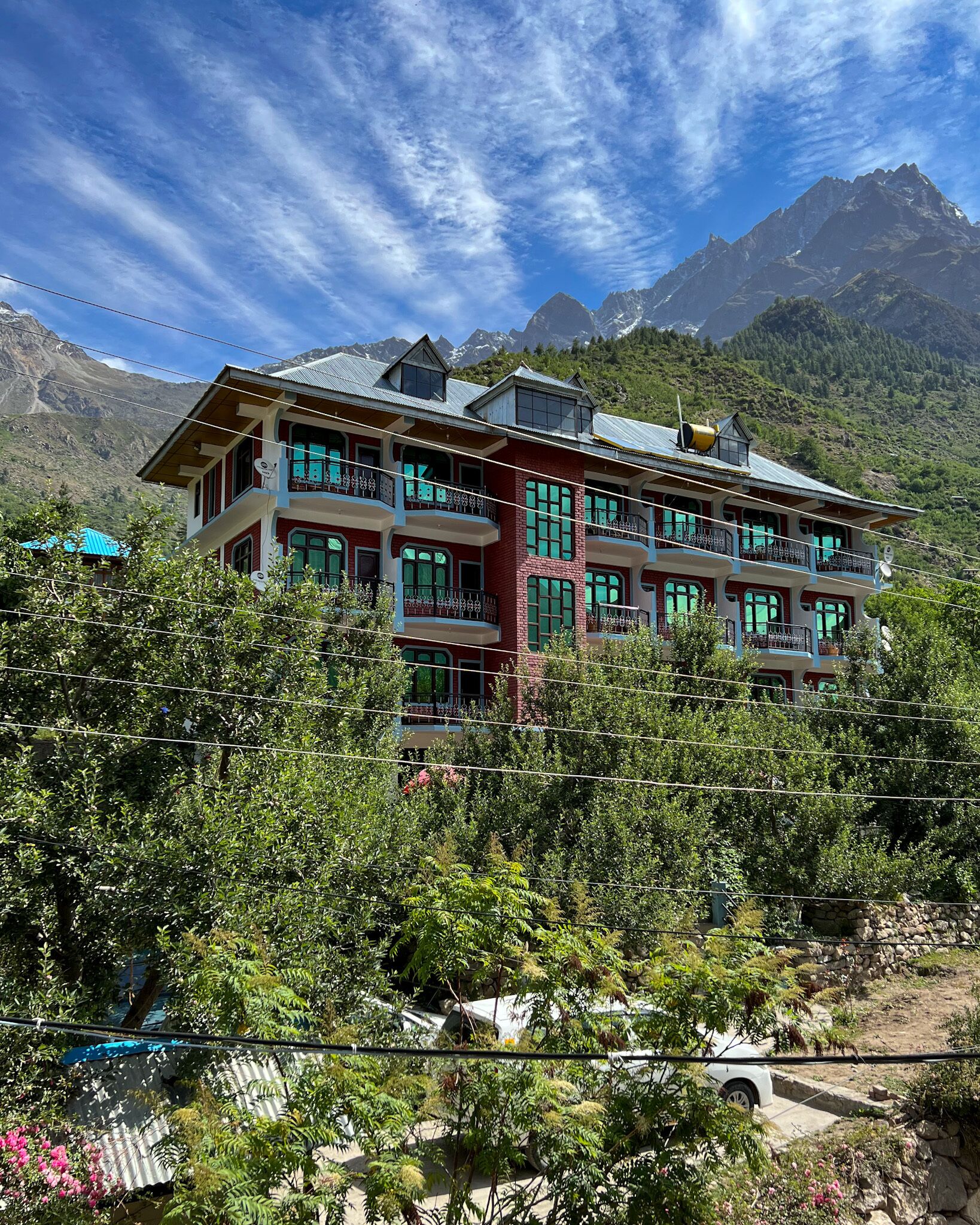 A multi-story building with balconies, surrounded by lush greenery and mountains in the background.