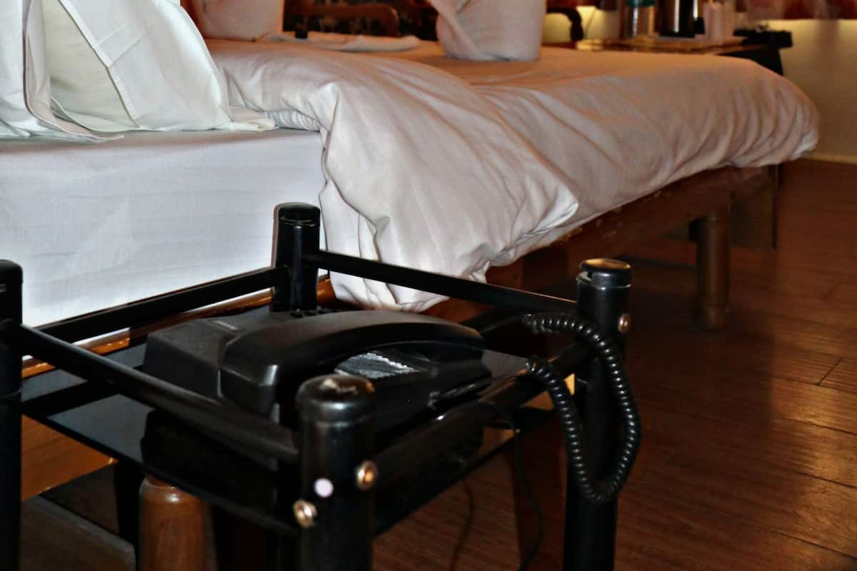 A hotel room with a bed, pillows, a bedside table with a telephone, a television, and curtains.