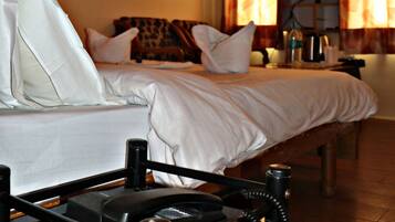 A hotel room with a bed, pillows, a bedside table with a telephone, a television, and curtains.
