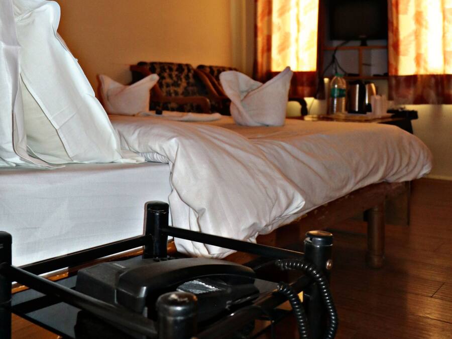 A hotel room with a bed, pillows, a bedside table with a telephone, a television, and curtains.
