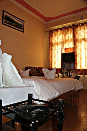 A hotel room with a bed, pillows, a bedside table with a telephone, a television, and curtains. - Hotel Prakash Regency Sangla (Sangla)