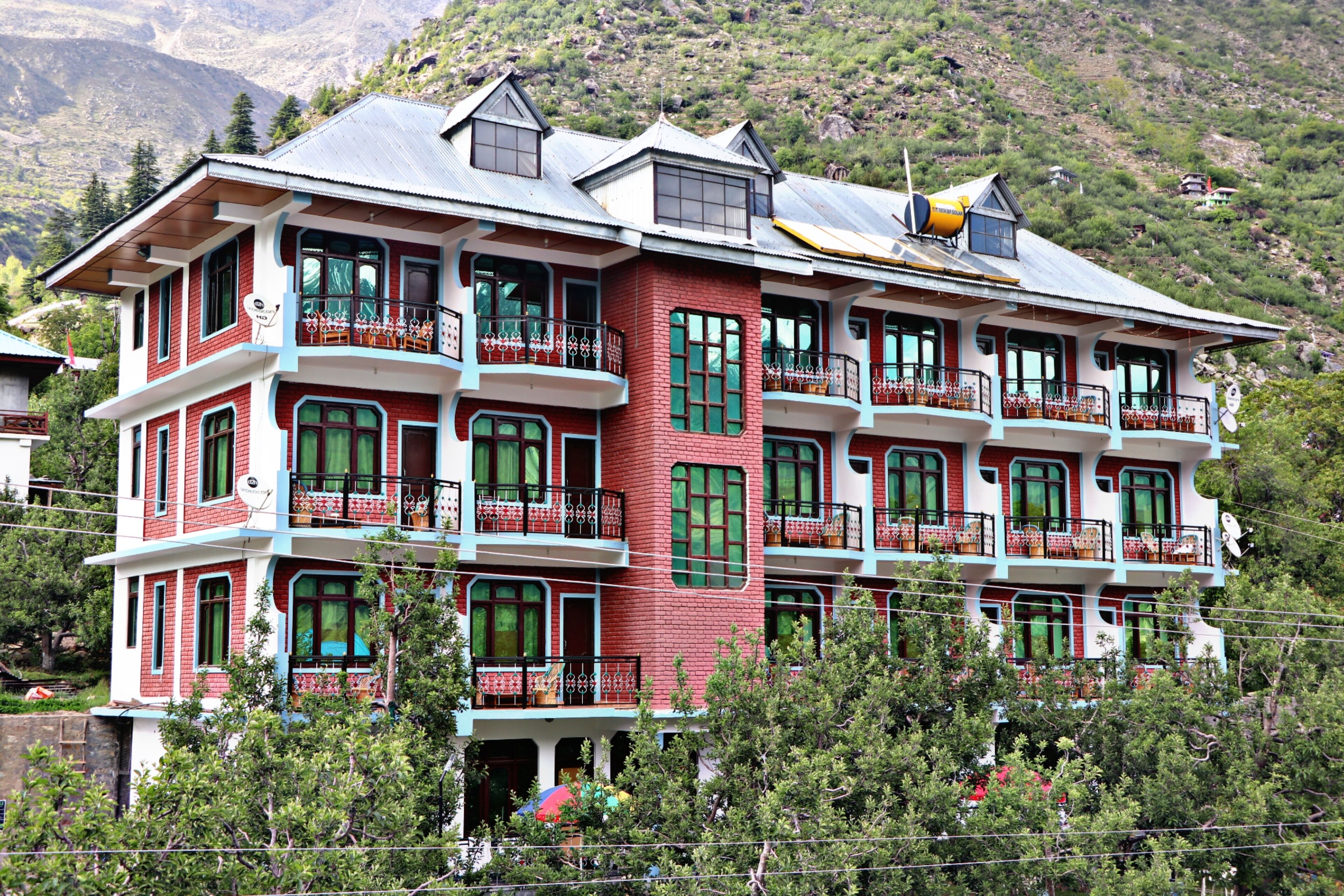 A multi-story building with balconies, surrounded by trees and mountains.