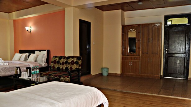 A hotel room with a bed, a chair, a desk with a kettle, and a wardrobe. - Hotel Prakash Regency Sangla (Sangla)