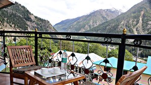 A balcony with a wooden table and chairs, a bottle of Bisleri water, and a view of snow-capped mountains. - Hotel Prakash Regency Sangla (Sangla)