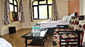 A hotel room with a bed, a sofa, a TV, and a table with water bottles. - Hotel Prakash Regency Sangla (Sangla)