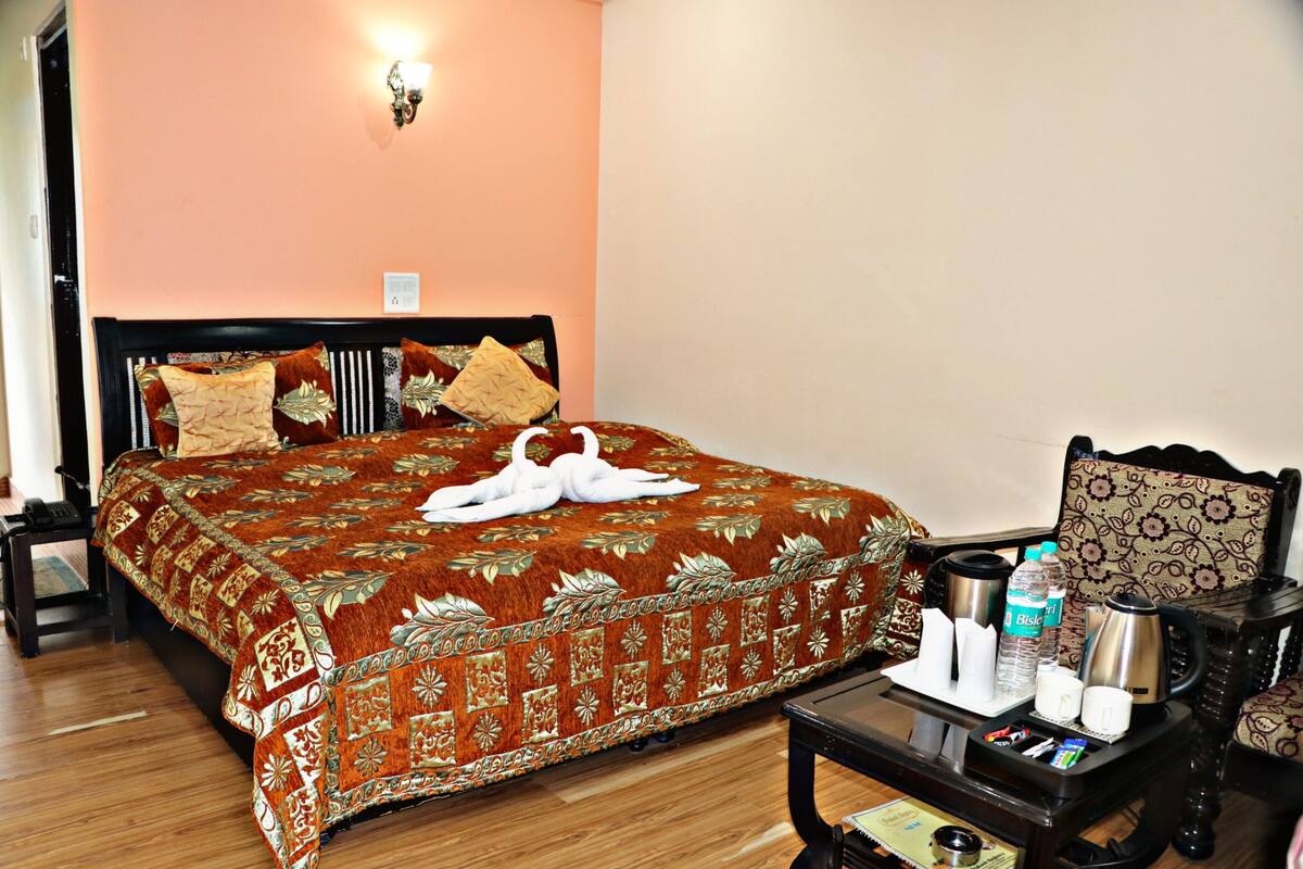 A hotel room with a large bed, a bedside table with a kettle, a bottle of water, and a cup.