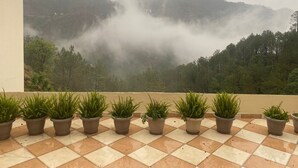 Un balcón con plantas en macetas y vistas a una cadena montañosa boscosa cubierta de niebla.
