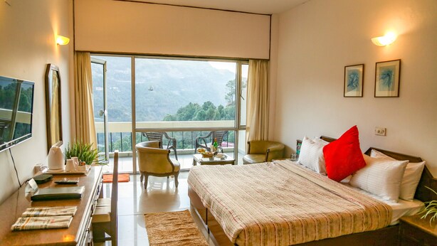 Un dormitorio con una cama grande, un escritorio, una silla y un balcón con vistas a las montañas.