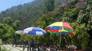Terraza al aire libre con sombrillas y sillas, rodeada de follaje y un paisaje montañoso.