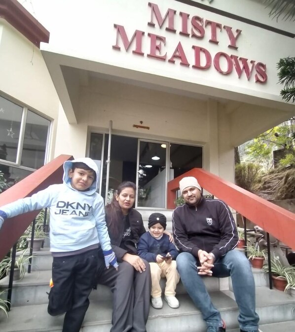 Una familia de cinco sentada en los escalones frente a un edificio con un letrero que dice 'Misty Meadows'.