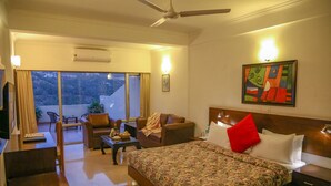 Una habitación de hotel con cama, sofá, mesa de comedor y balcón con vistas.