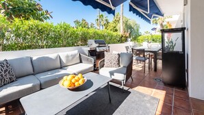 Une terrasse extérieure avec un canapé, des chaises, un barbecue et une table.