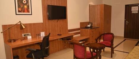 Une chambre d’hôtel avec un bureau en bois, un fauteuil de bureau noir, une chaise rouge, un téléviseur fixé au mur et une armoire en bois.