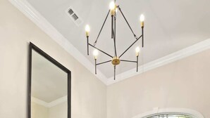 A hallway with a wooden floor, a large mirror, a modern chandelier, and a white door with stained glass windows. - Poolside Place - Game Room - MTB-Friendly (Bentonville)