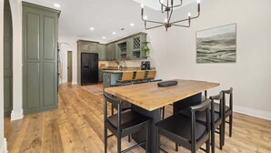A modern kitchen with green cabinets, a wooden dining table, and black chairs. - Poolside Place - Game Room - MTB-Friendly (Bentonville)