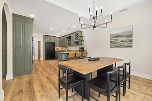 A modern kitchen with green cabinets, a wooden dining table, and black chairs. - Poolside Place - Game Room - MTB-Friendly (Bentonville)