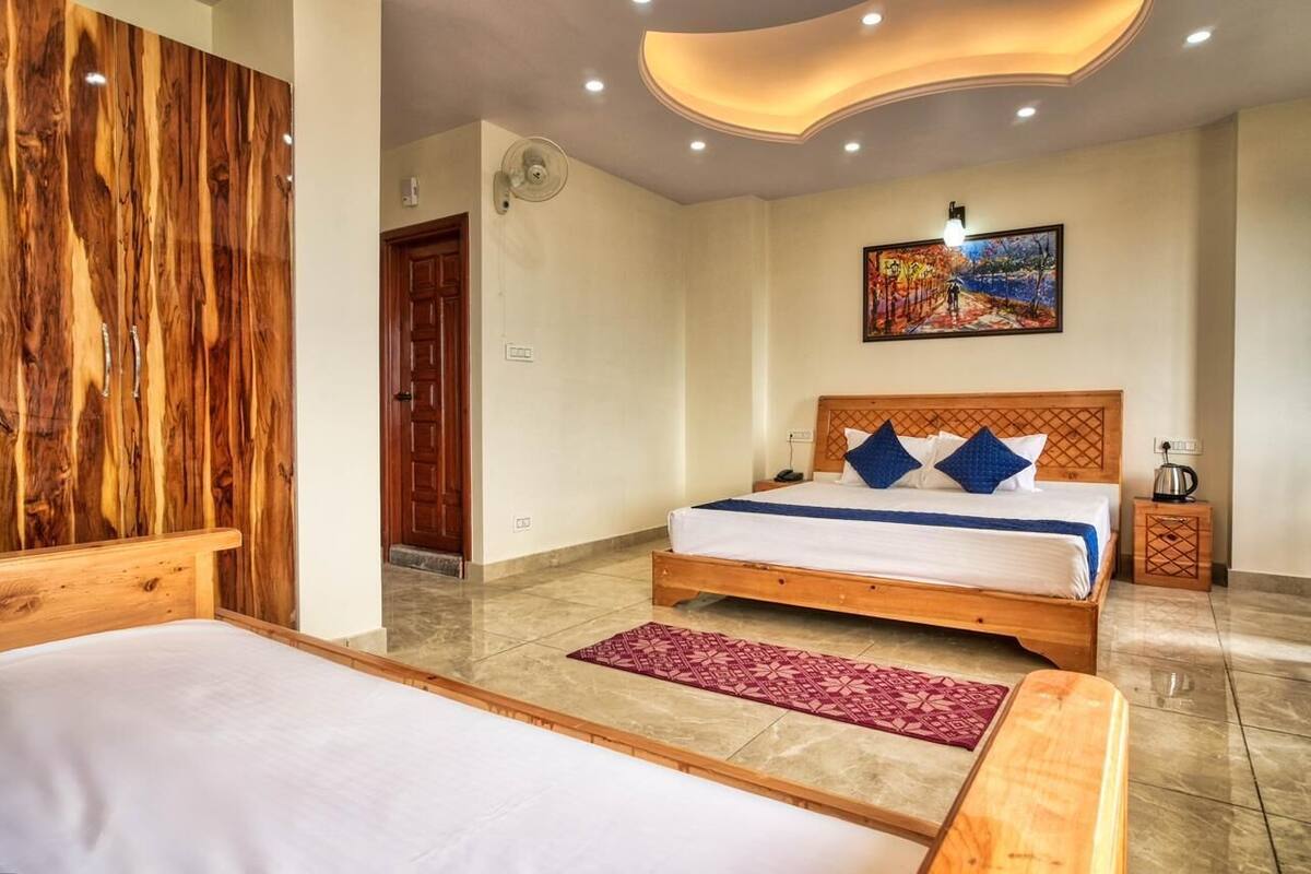 Un dormitorio con cabecera de madera, cama con ropa de cama azul y blanca, alfombra roja estampada y un cuadro en la pared.