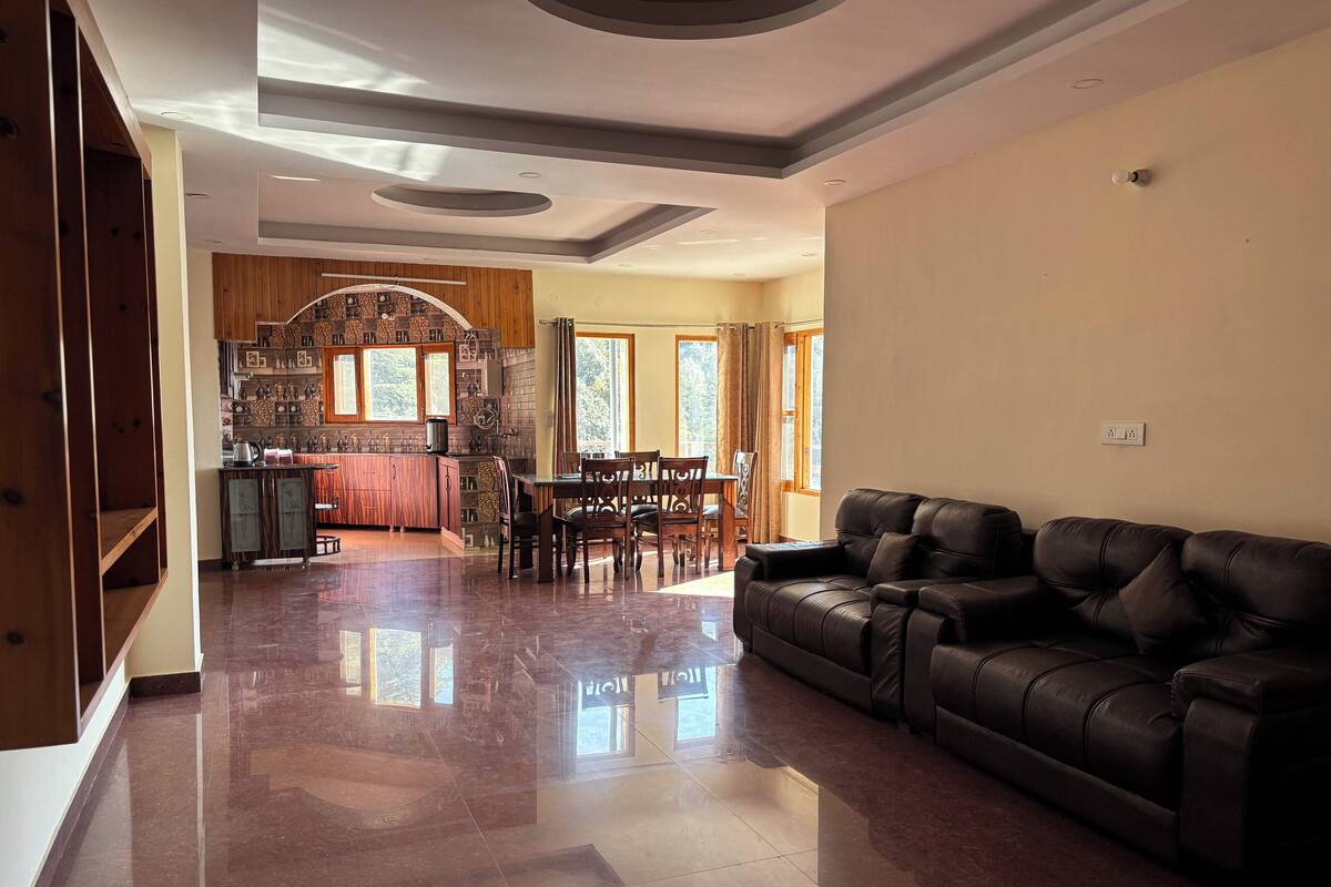 Un amplio salón con un sofá de cuero, una mesa de comedor con sillas y una cocina con armarios de madera y salpicadero de piedra.