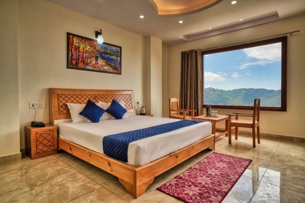 Un dormitorio con una cama de madera, una mesita de noche, una silla, un escritorio, un ventanal con vistas a la montaña y un cuadro en la pared.