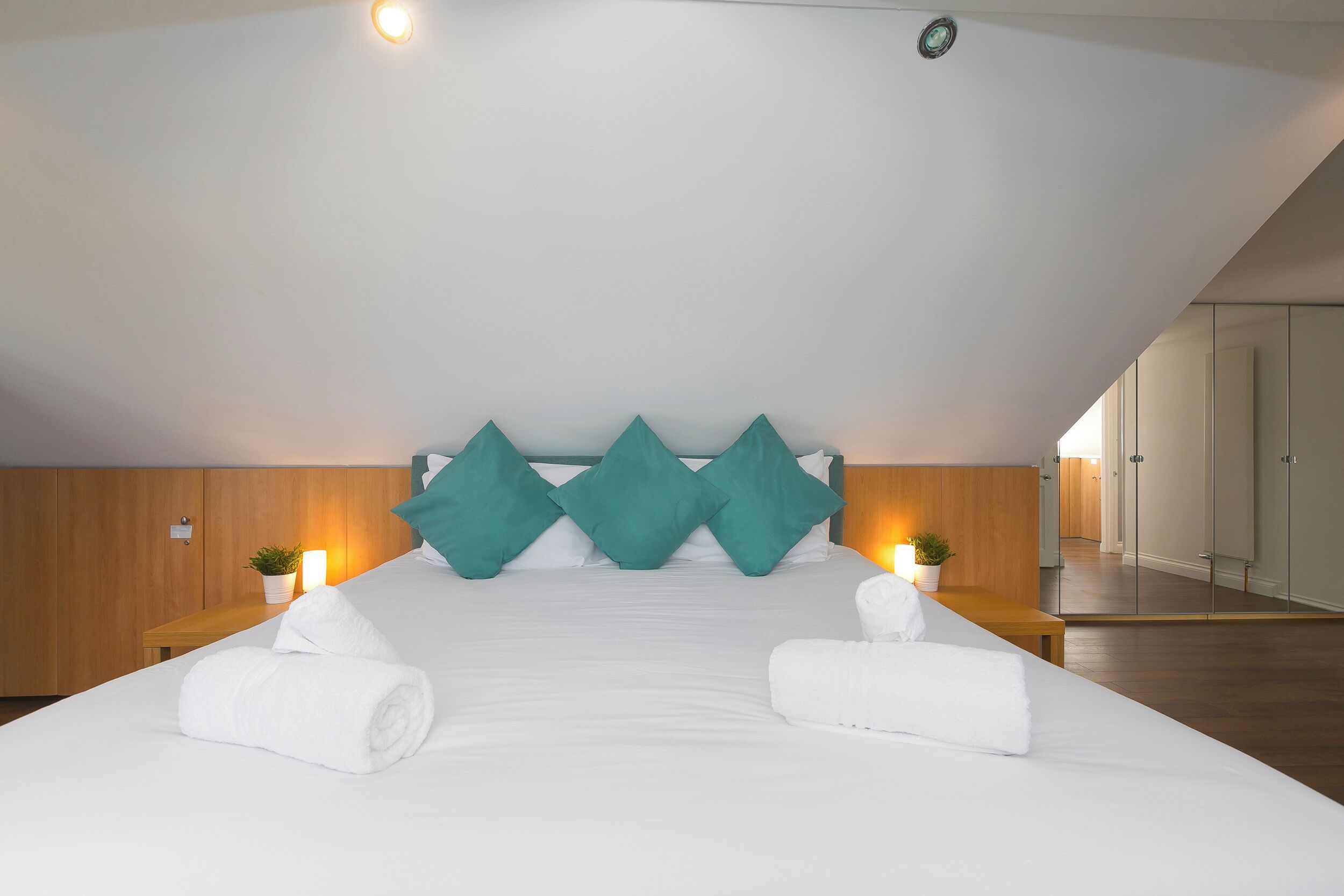 A modern hotel room with a large bed, teal pillows, and two bedside tables with lamps.