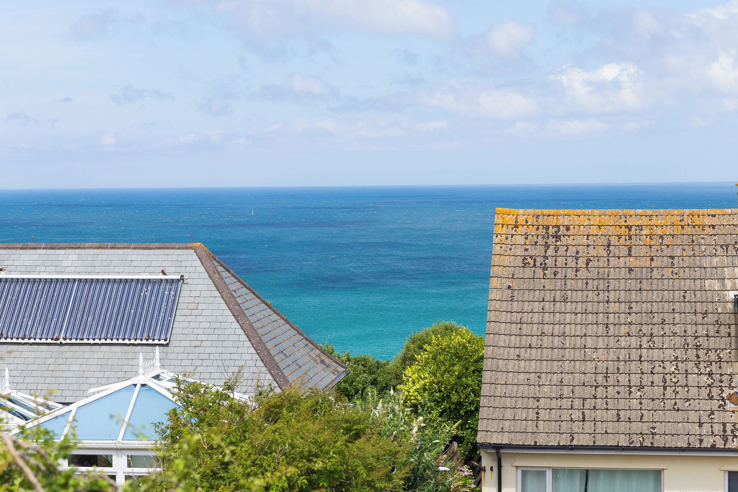 Eine Küstenansicht mit Meer und einem Gebäude mit Ziegeldach und Solarpanel.