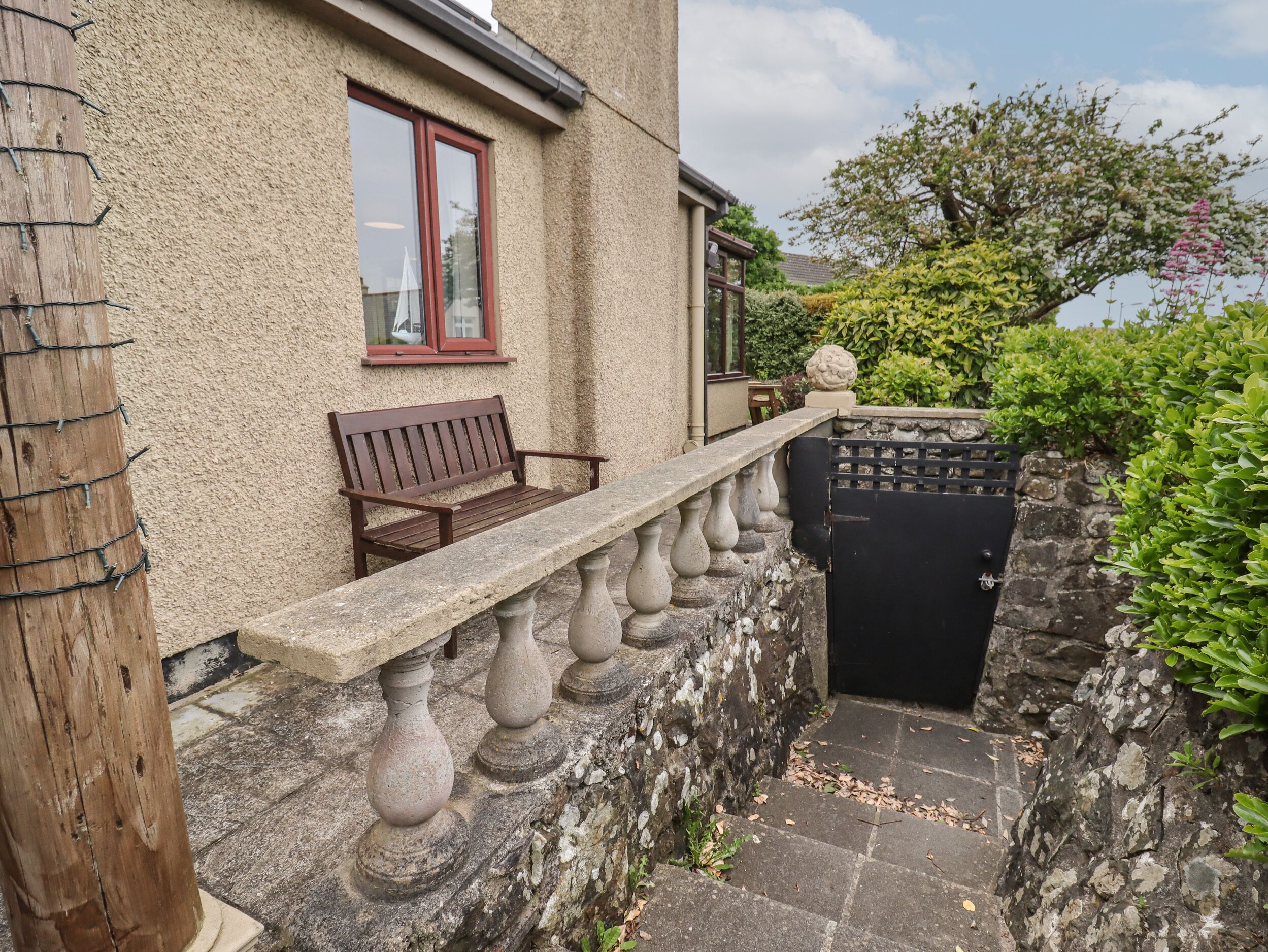 A stone balustrade with a bench, a black gate, and a stone wall.