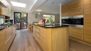 A modern kitchen with wooden cabinets, a central island, and built-in appliances. - Spernenwyn (St Ives)
