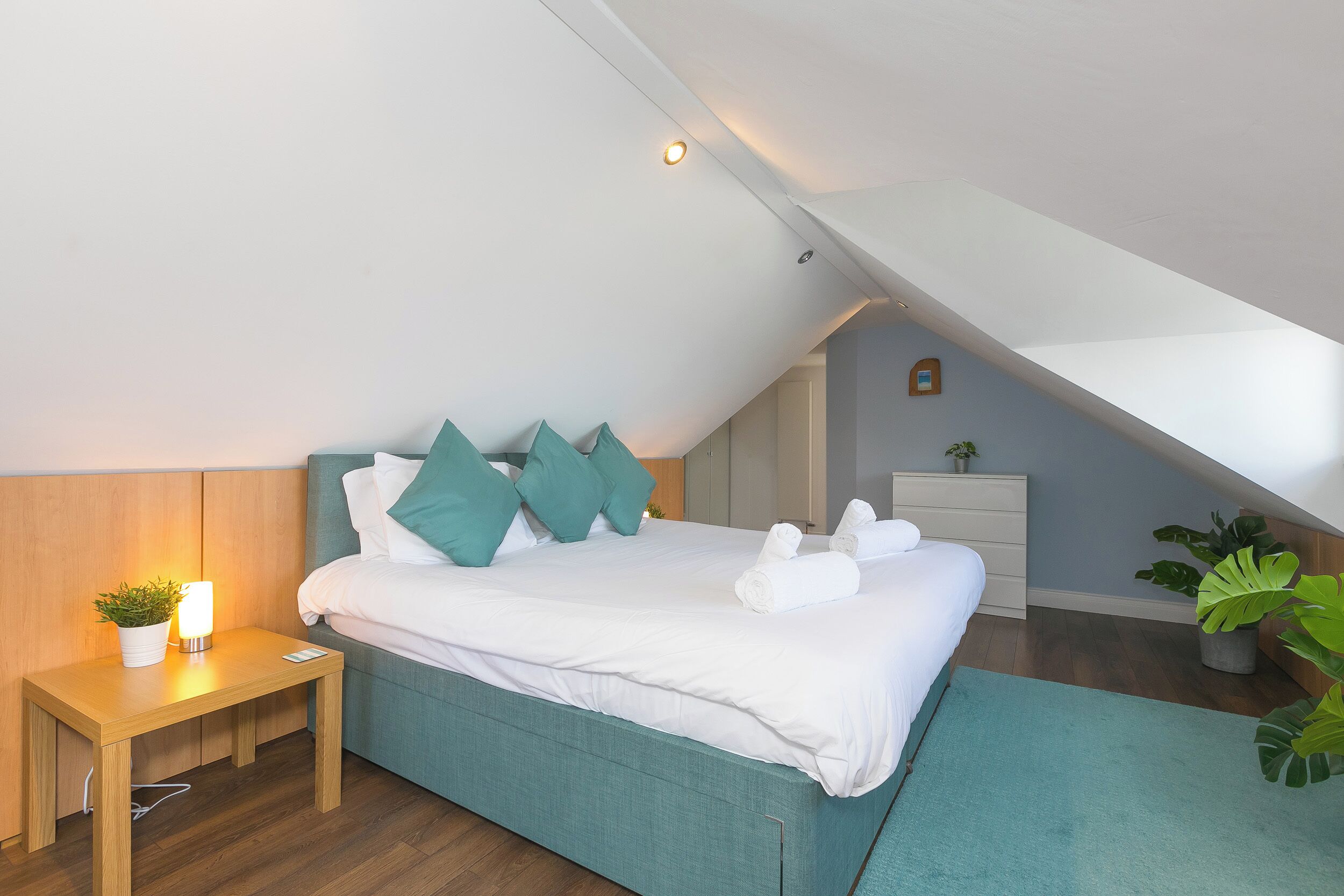 A bedroom with a bed, bedside table, and a nightstand with a lamp.